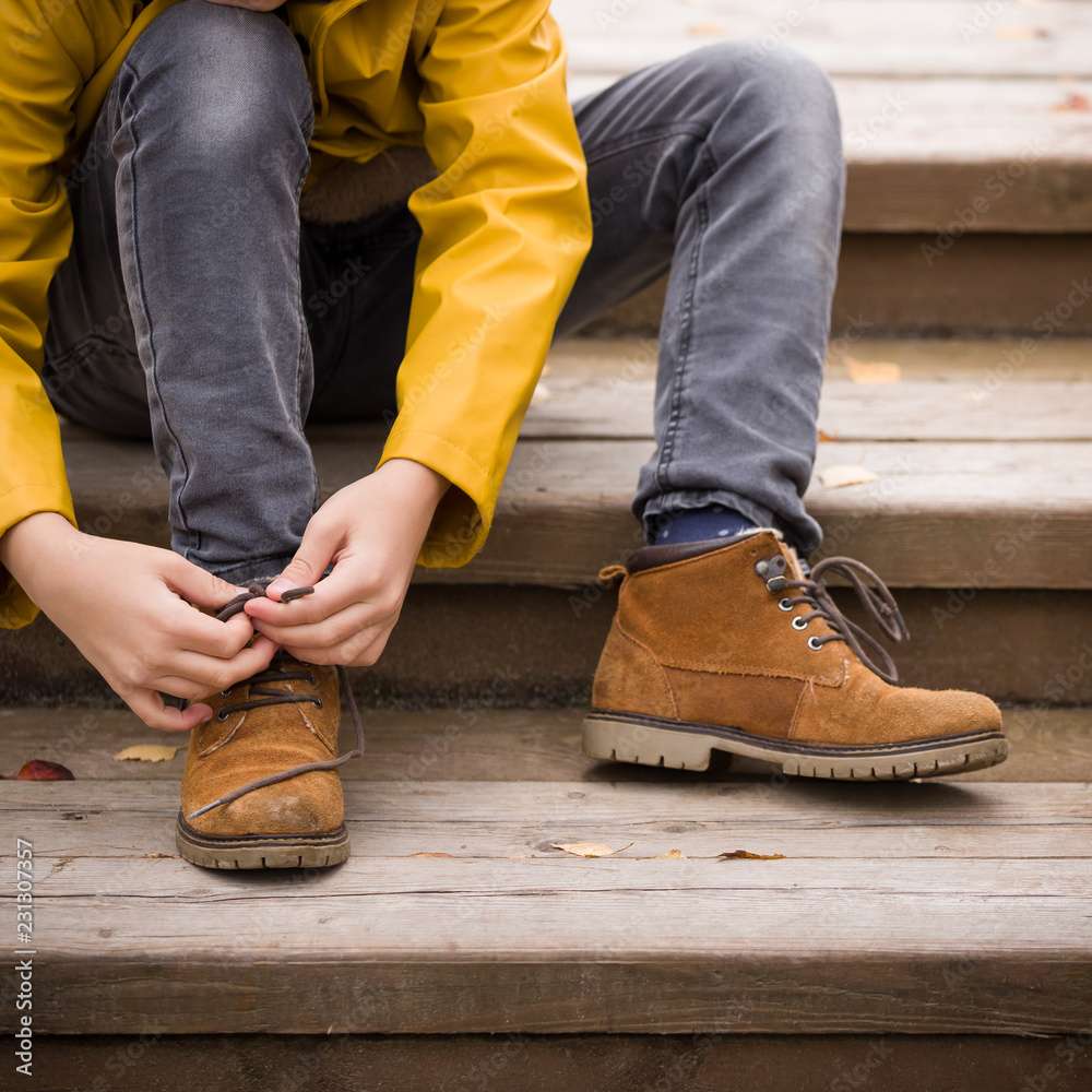 Closeup of cute child tying laces while walking in the city park on a cold autumn day. - obrazy, fototapety, plakaty 
