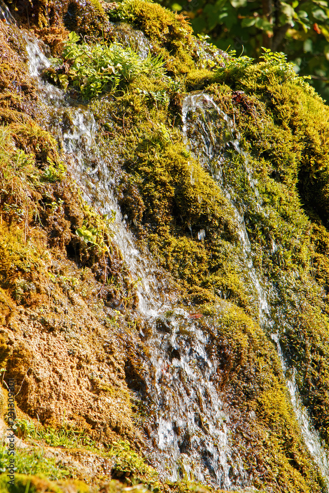 Beautiful small waterfall on the background of green moss. Summer sunny weather Beautiful small waterfall on the background of green moss. Summer sunny weather