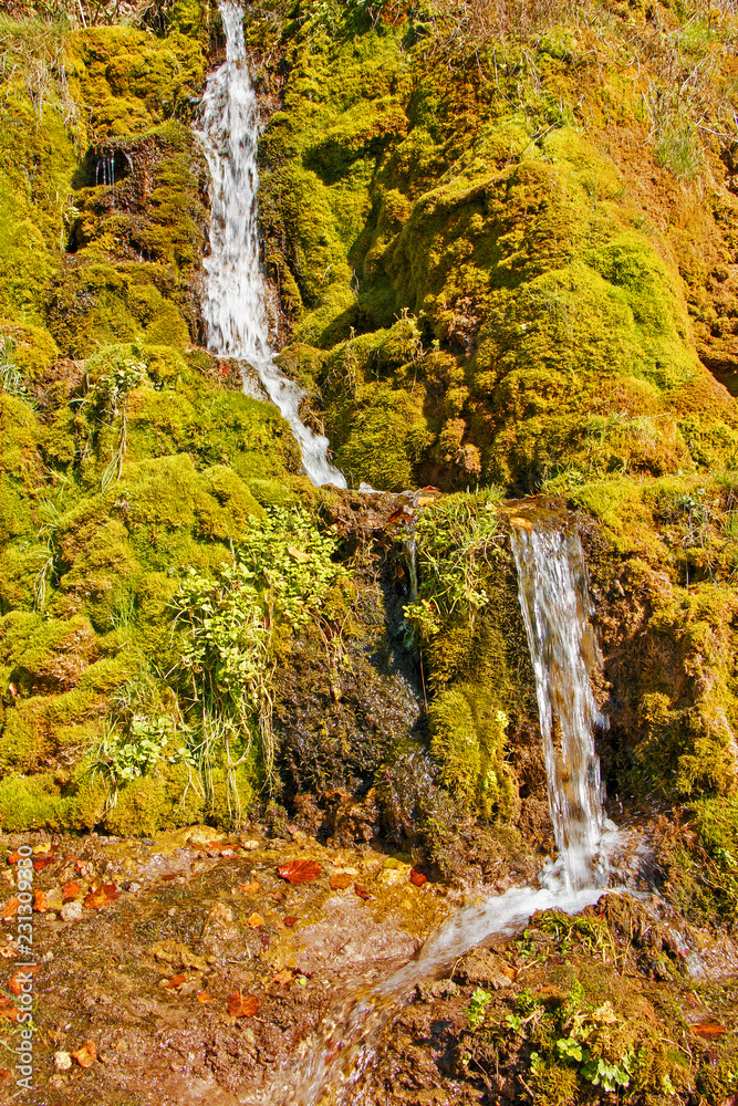 Beautiful small waterfall on the background of green moss. Summer sunny weather Beautiful small waterfall on the background of green moss. Summer sunny weather