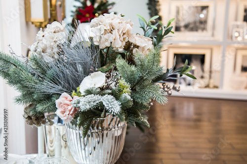 Decorated vase with beautiful white flowers and christmas tree branches, bright interior with decorations on the background