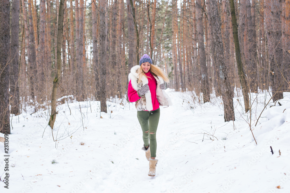 Season, nature, people concept - a beautiful blond woman running in winter wood and smiling