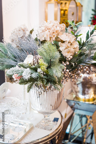 Decorated vase with beautiful white flowers and christmas tree branches, bright interior with decorations on the background