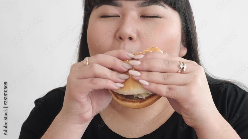 the girl of Asian appearance eats a Burger and enjoys the taste. not a healthy diet for young people the girl of Asian appearance eats a Burger and enjoys the taste. not a healthy diet for young people