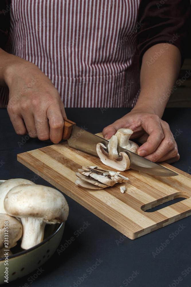 woman in apron cuts mushrooms on a board with a knife