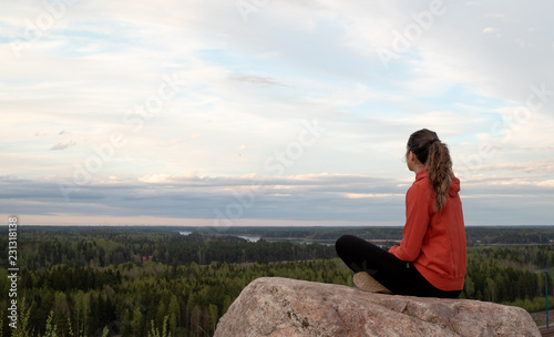 Young beautiful woman doing yoga and mindfulness exercises, while sitting on the edge of a hill and staring to the sunset horizon. photo