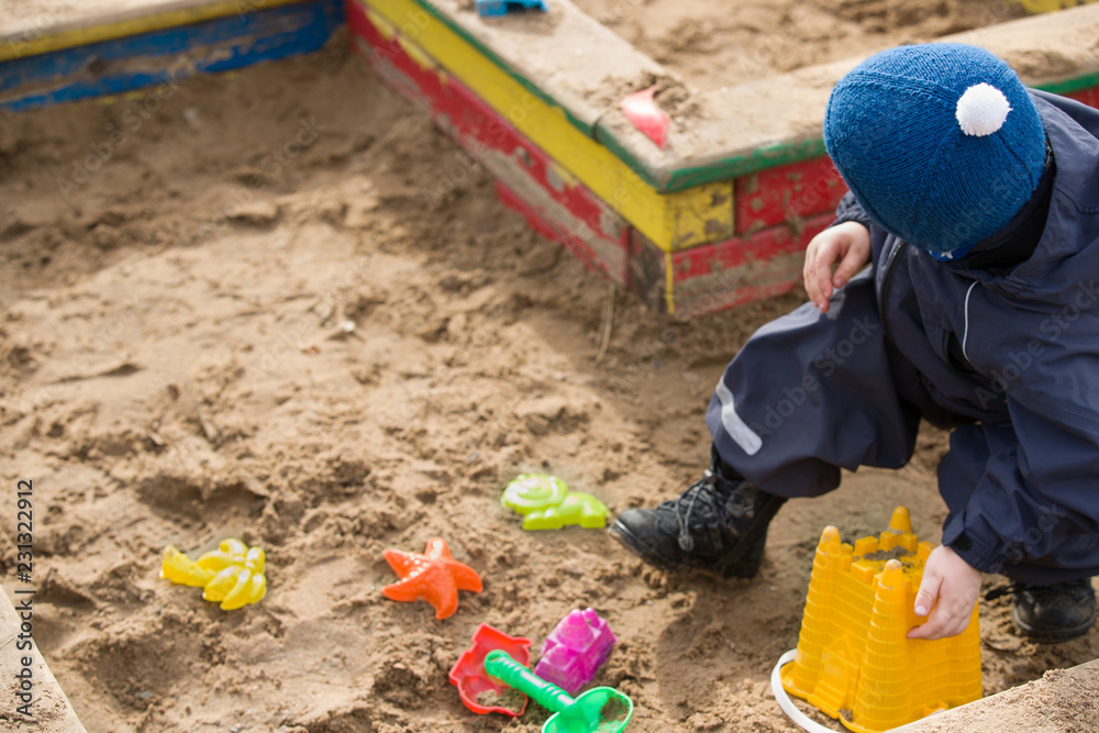Little toddler boy sitting on the sand and playing with plastic toys and sand on a playground. Little toddler boy sitting on the sand and playing with plastic toys and sand on a playground.