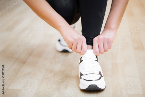 Physical activity. Close-up of girl tying shoelaces on sports shoes in gym
