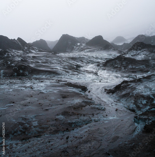 Runlet of glacier water floating between small ash covered ice hills, Fimmvorduhals, Iceland.