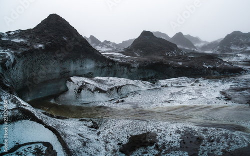 Runlet of glacier water floating between small ash covered ice hills, Fimmvorduhals, Iceland.