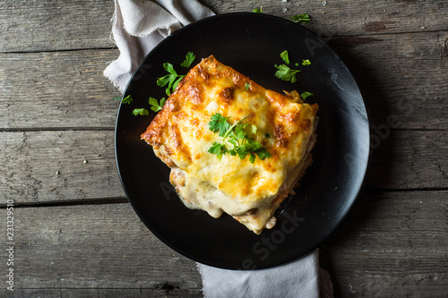 Piece of tasty hot lasagna with red wine. Small depth of field. Traditional italian lasagna. Portion. Italian food. Food on black plate. Bolognese sauce. Bechamel sauce. Still life of food. photo