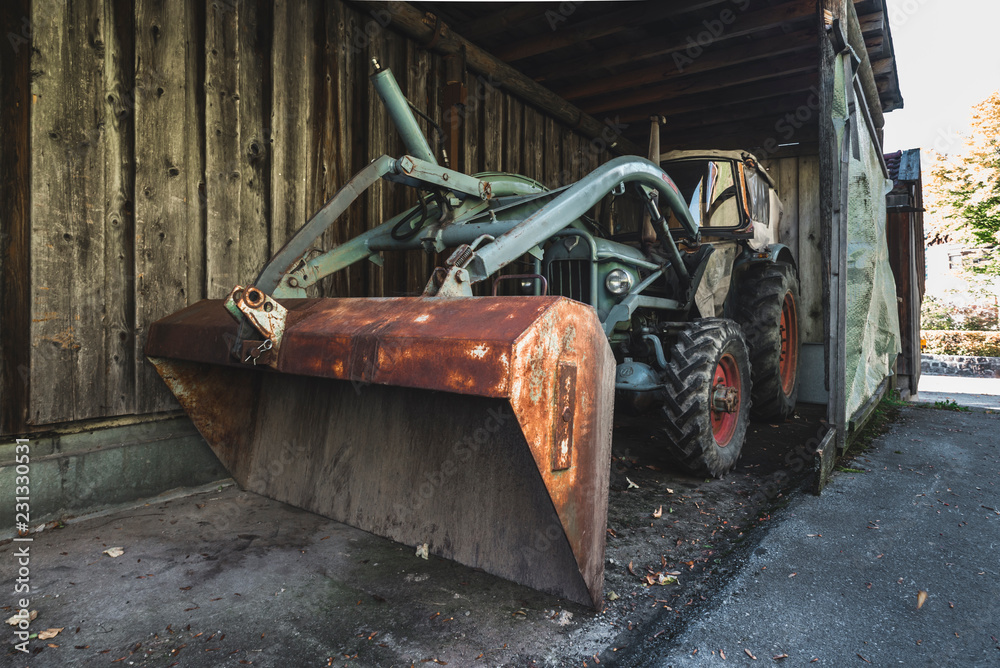Naklejka premium Alte Eicher Zugmaschine mit Hubarm und Schaufel in einem dunklen Holzschuppen, Bayern, Deutschland