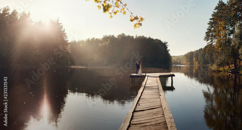 Lake of love, romantic young couple standing on the dock at the lake. Autumn sunset in the forest lake