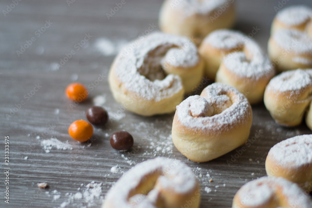Rolls sprinkled with powdered sugar and candy on the table with a wooden texture.