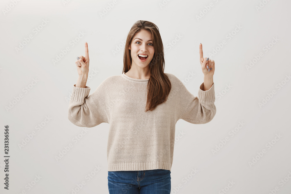 Soon we will be in plane, travelling to warm countries. Portrait of excited beautiful caucasian brunette pointing up while being thrilled with good news, showing direction over gray background Soon we will be in plane, travelling to warm countries. Portrait of excited beautiful caucasian brunette pointing up while being thrilled with good news, showing direction over gray background