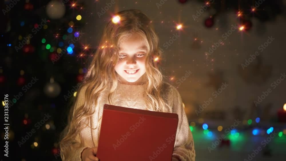 Adorable blond girl opening gift box, magic Christmas atmosphere, glowing effect