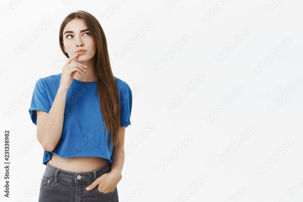 Creative smart and thoughtful attractive european woman in trendy blue cropped top making hmm gesture with finger on lower lip raising eyebrow and gazing up, thinking making choice in mind Creative smart and thoughtful attractive european woman in trendy blue cropped top making hmm gesture with finger on lower lip raising eyebrow and gazing up, thinking making choice in mind