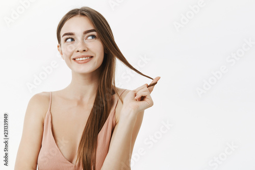 Flirty woman having naughty thoughts in mind rolling lock of hair on finger and smiling curiously with some intention thinking or dreaming gazing at upper right corner with delighted smile