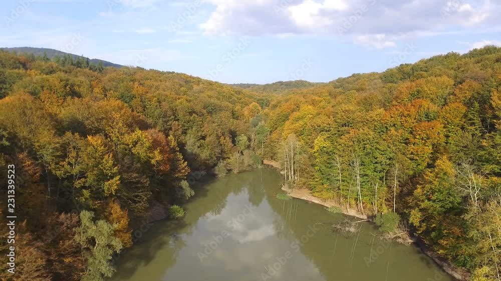 Aerial drone view above the pond in the colorful beech forest in autumn. Flying above the water. Aerial drone view above the pond in the colorful beech forest in autumn. Flying above the water.