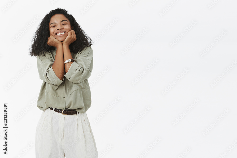 Delighted cute and tender pleased african american girlfriend in trendy shirt and pants leaning face on palms and smiling delighted from joy and happiness recalling nice moment over gray background Delighted cute and tender pleased african american girlfriend in trendy shirt and pants leaning face on palms and smiling delighted from joy and happiness recalling nice moment over gray background