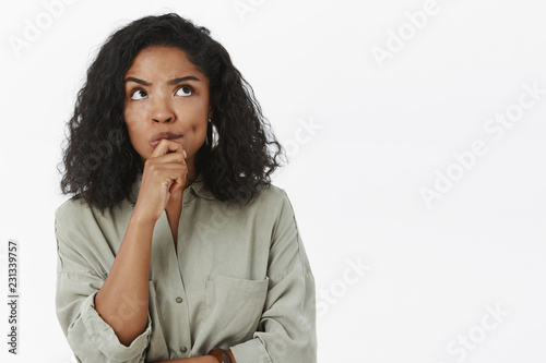 Girl needs make up excuse thinking standing focused in thoughtful pose holding hand on chin frowning looking up posing over gray background determined and concentrated on thought