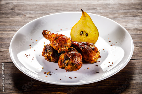 Grilled chicken drumsticks with pear on wooden background
