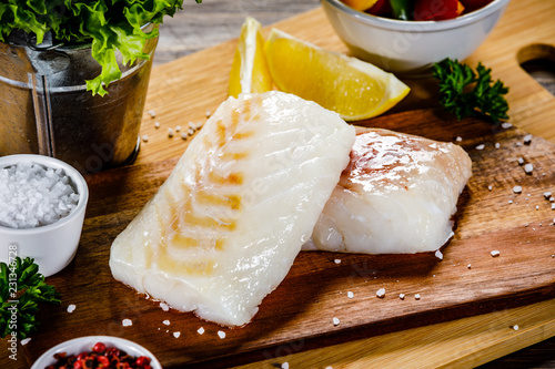 Fresh raw cod with herbs and vegetables served on cutting board on wooden table