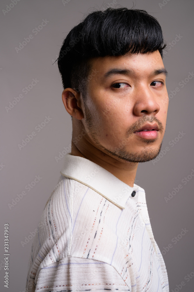 Portrait of young Asian man against gray background