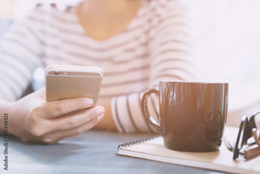 close up people female sit using mobile smartphone in take a break relax. cup coffee on desk table with book notepad,eyeglasses, equipment supplies in the work. copy space. concept working woman. close up people female sit using mobile smartphone in take a break relax. cup coffee on desk table with book notepad,eyeglasses, equipment supplies in the work. copy space. concept working woman.