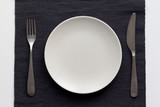 Fork, knife and dish on the black tablecloth on the white background. Top view, flat lay, copy space, mock up