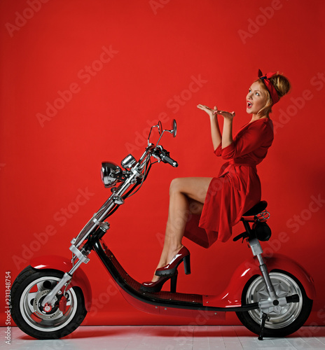 Woman pinup style ride new electric car motorcycle bicycle scooter present for new year 2019 in red dress pointing hands up