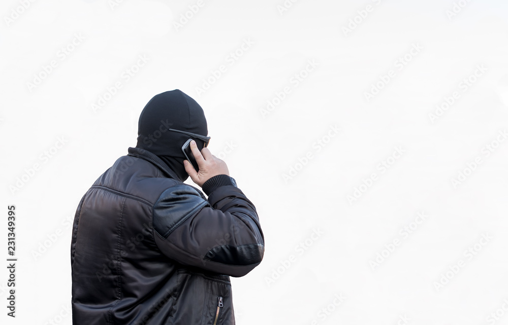 a man, a terrorist, a bandit in a black leather jacket and a mask talking on the phone