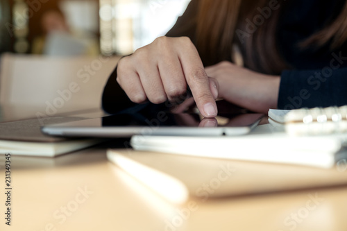 Closeup image of hand pointing at a black tablet pc screen with notebook on wooden table