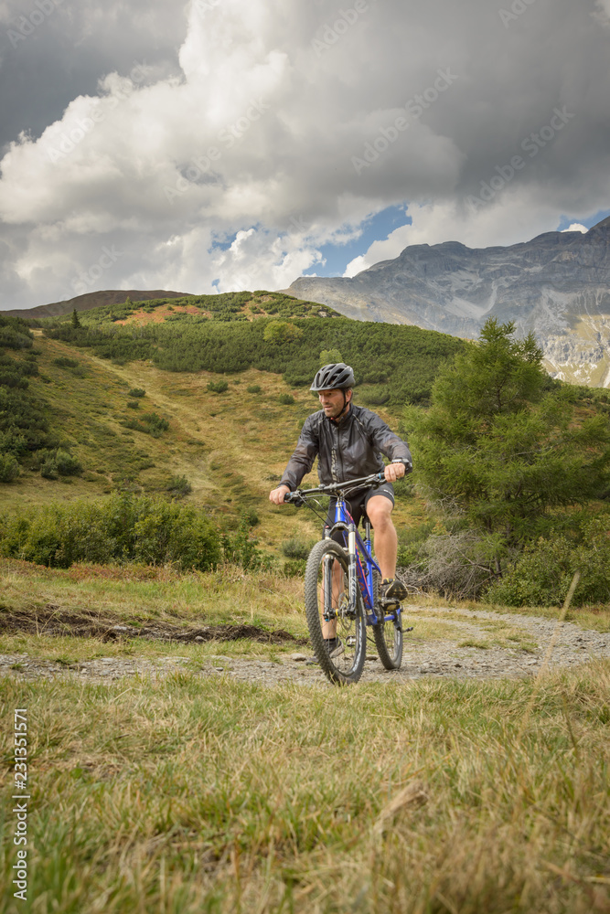 Fototapeta premium Mountain biker on the mountain pasture with mountains and blue sky as a background, traveling alone, on the corona time, 
