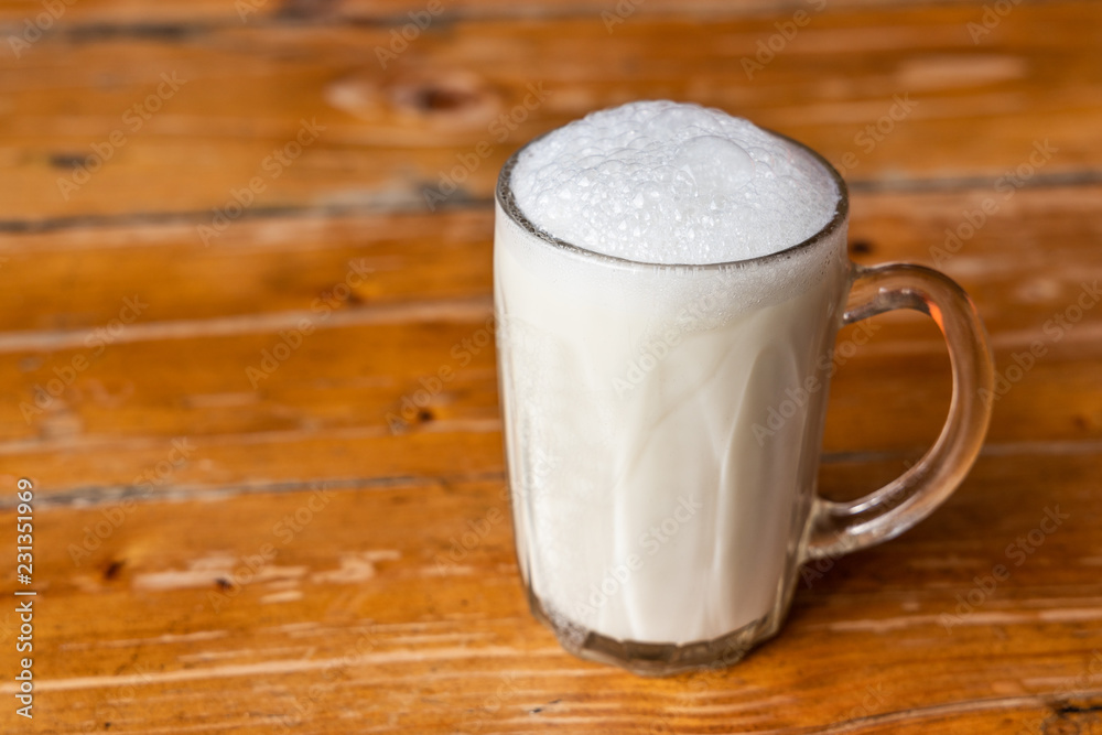 Glass of warm fresh milk with froth on wooden table top Glass of warm fresh milk with froth on wooden table top