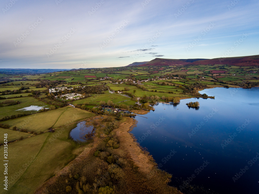 Aerial panoramic view of a beautiful natural lake in Brecon Beacons surrounded by rural farmland (Llangorse Lake, Wales)