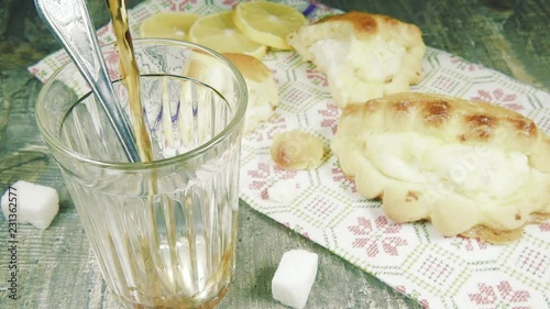 Slow motion pour hot tea into a faceted glass with an aluminum teaspoon with a curd pie sochnik photo