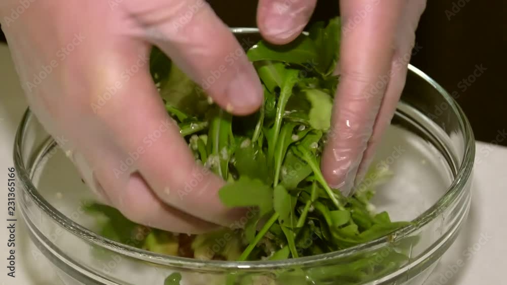 The cook mixes the salad with his hands. Assistant cook pours salad dressing. Salad consists of arugula leaves, avocado, quinoa croup. The cook mixes the salad with his hands. Assistant cook pours salad dressing. Salad consists of arugula leaves, avocado, quinoa croup.