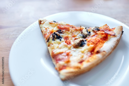 Slice of pizza with mushrooms, cheese and ham lying on a white plate