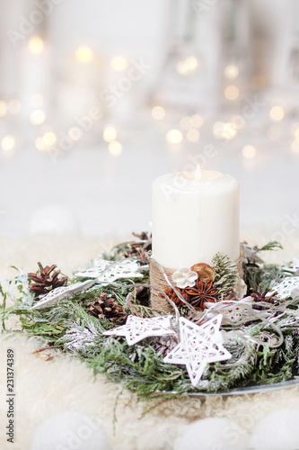Christmas candles and snowy fir branches over white wooden background with lights.  New Year's decoration with a fir tree in white tones.