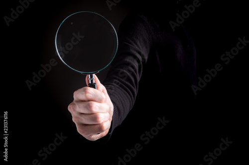 Man's hand, holding classic styled magnifying glass on a black background
