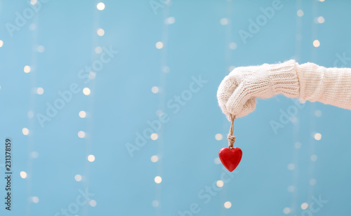 Hand holding a heart ornament on a shiny light blue background