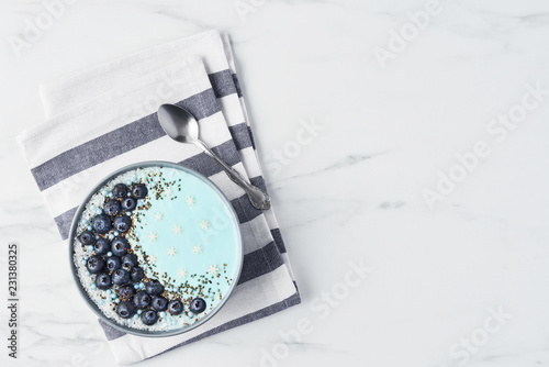 Top view of blue yogurt smoothie bowl made with blueberry, coconut flour, chia seeds and sugar pearls on white marble table with copy space. photo