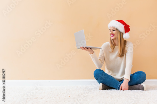 Young woman with santa hat using her laptop on a white carpet