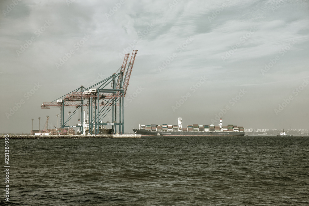 A large cargo ship enters an industrial cargo port with bridges of port marine cranes. Container ship, cargo ship, sea vessel in the sea fairway of the cargo port Odessa
