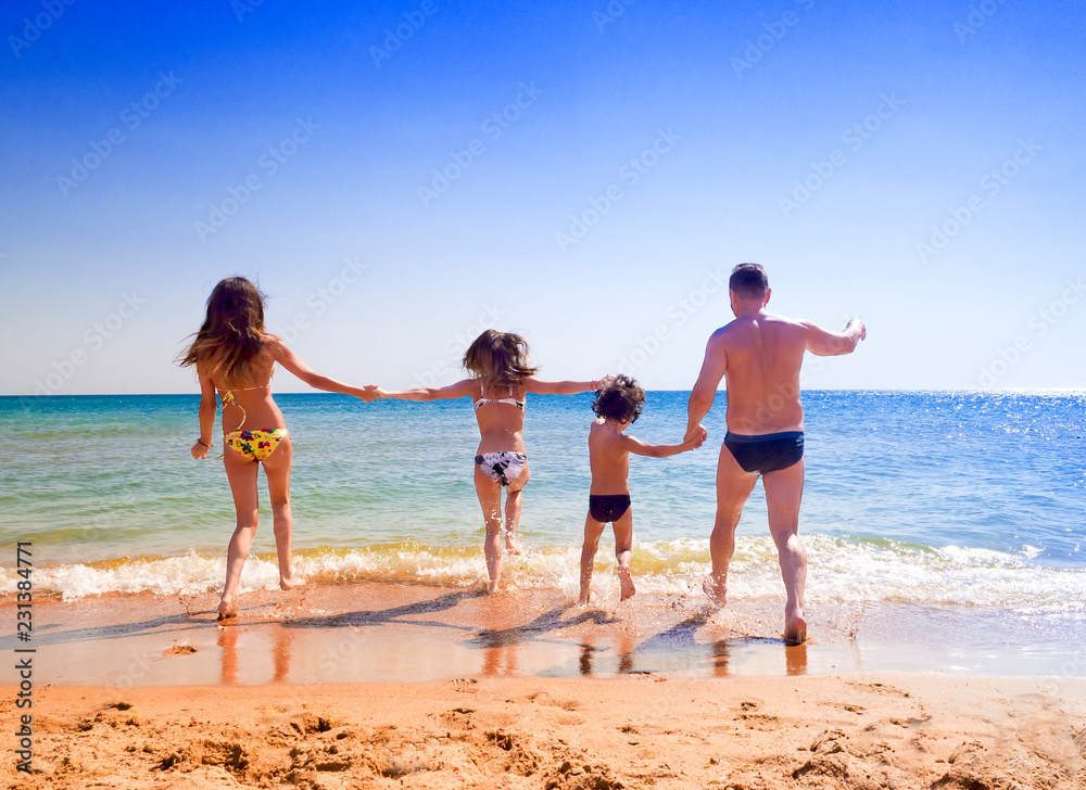 happy young family have fun on beach running into warm sea. Love and affection concept