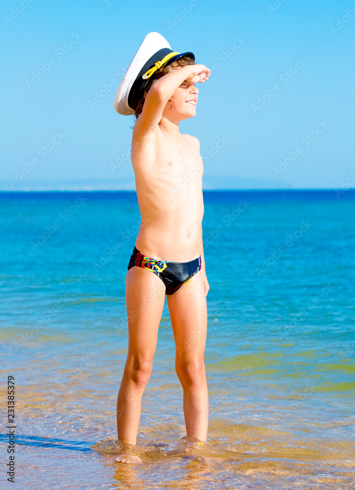 Funny child in black swimming trunks in a sea cap looking into the distance on the background of blue sea and sky Funny child in black swimming trunks in a sea cap looking into the distance on the background of blue sea and sky
