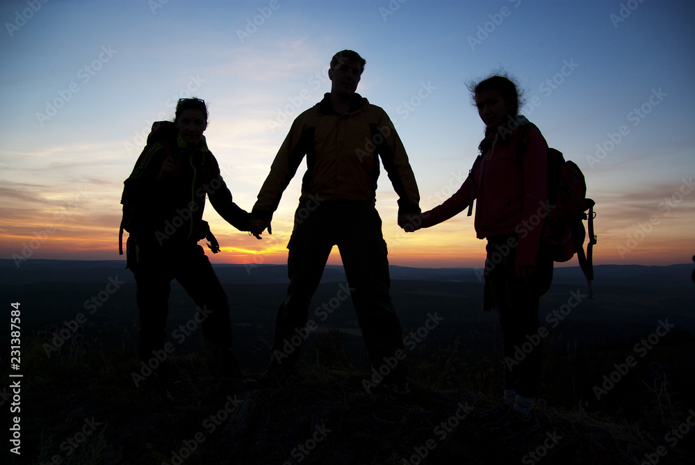 A group of tourists on top of a mountain at sunset.