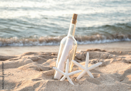 pair of tropical white starfish in beach sand with paper message in a bottle