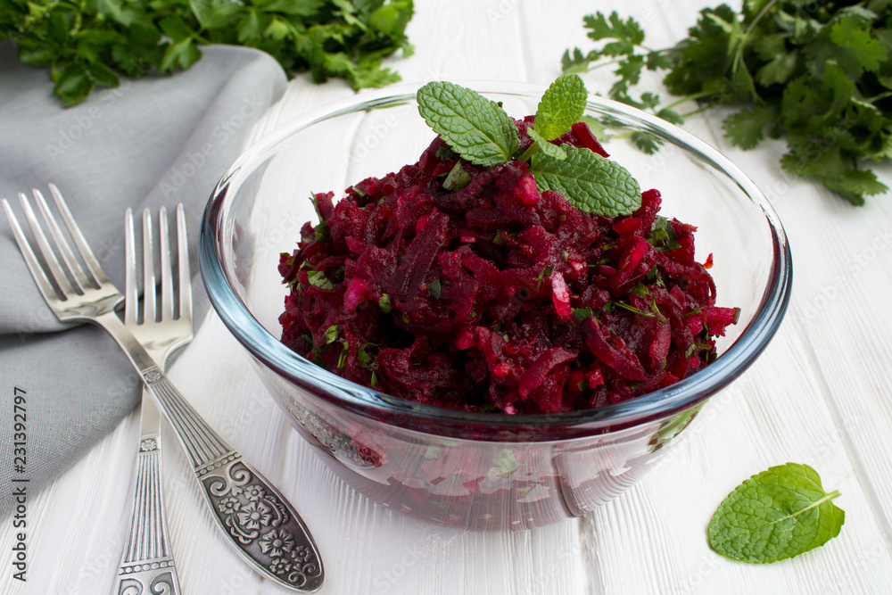 Salad with grated beets and herbs in the glass bowl on the white wooden background Salad with grated beets and herbs in the glass bowl on the white wooden background