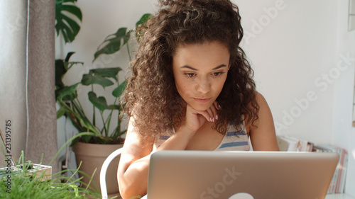 Charming young woman typing on laptop computer at home.
